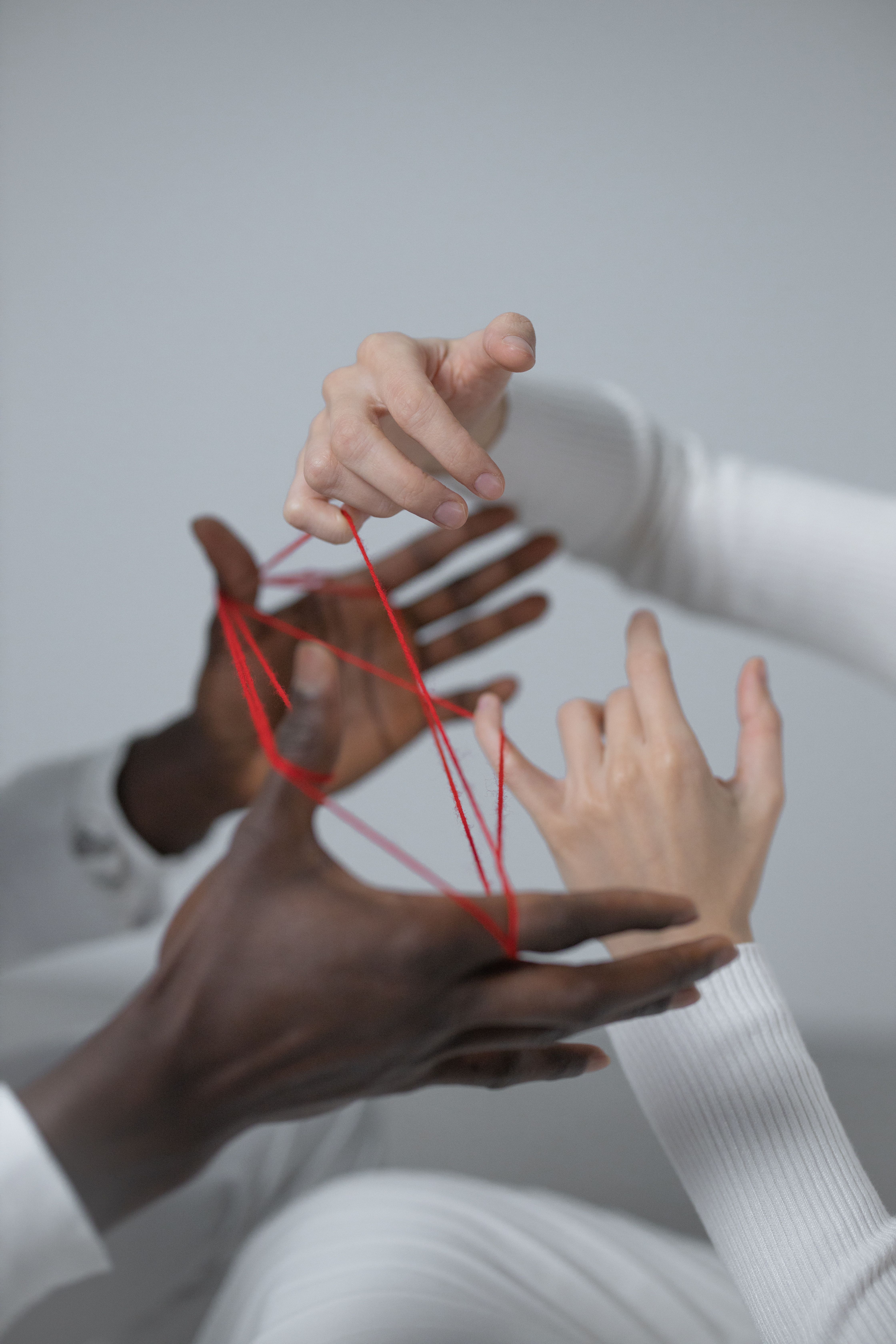 Close-up of diverse hands intertwined with red thread, symbolizing connection and unity.